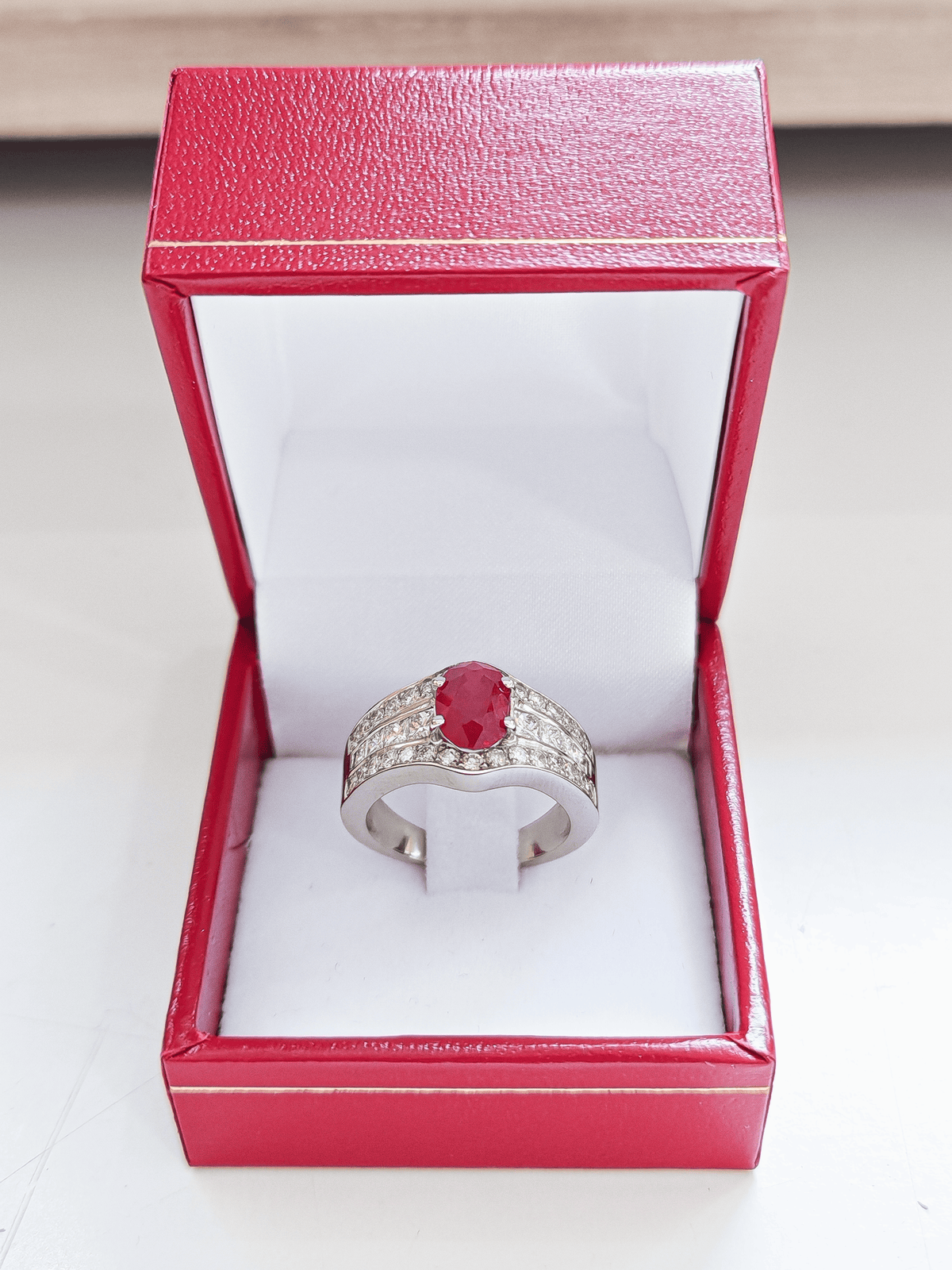 Bague en or blanc 18 carats sertie d'un rubis central et de diamants posée dans un écrin pour bague sur un fond blanc