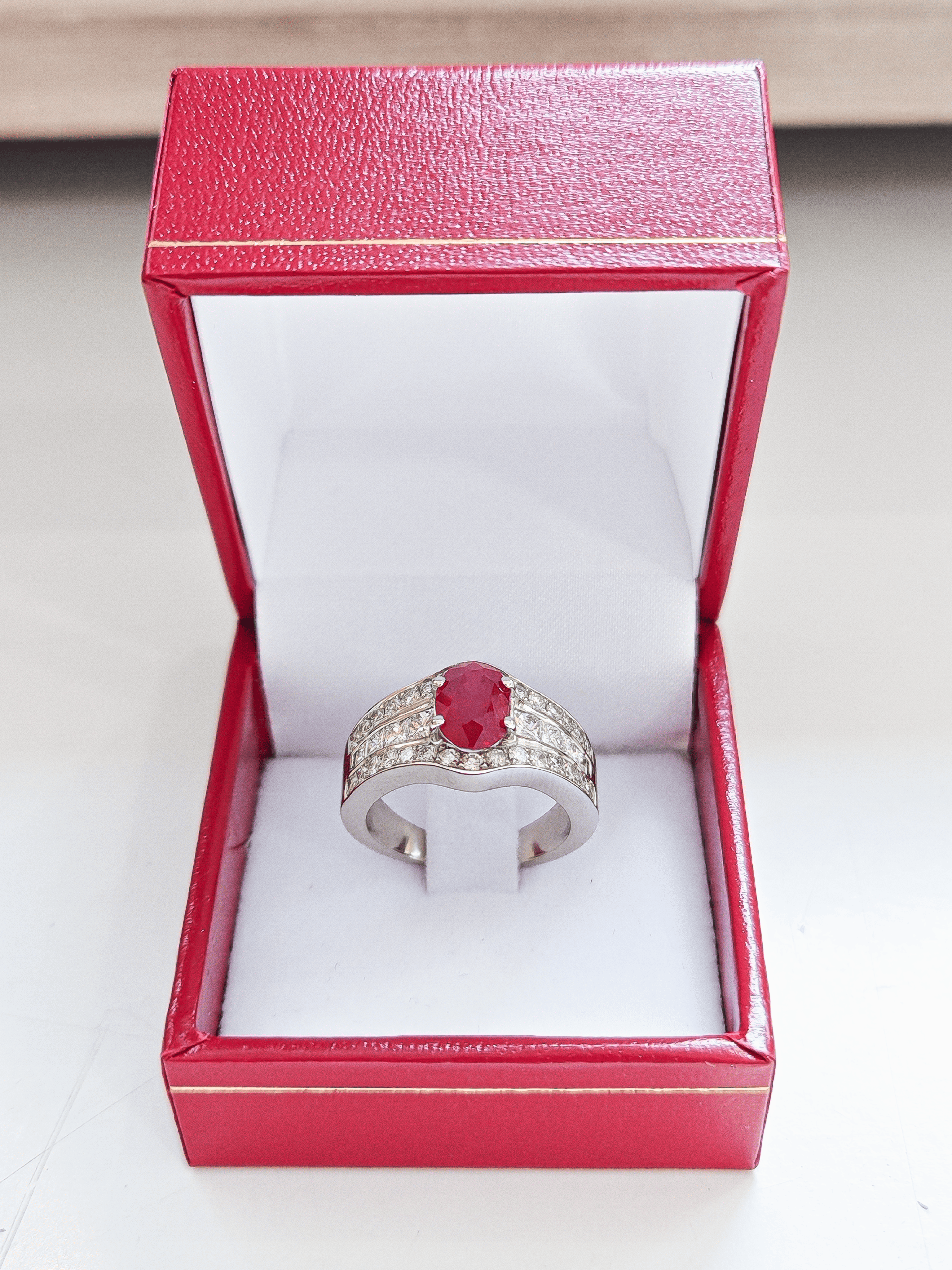 Bague en or blanc 18 carats sertie d'un rubis central et de diamants posée dans un écrin pour bague sur un fond blanc