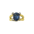 Bague en or jaune 18 carats, saphir ovale cabochon bleu nuit environ 5 carats en serti clos rail, 4 diamants ronds brillants serti lunette aux quatre angles du motif central sur corps fendu anatomique, vue de face