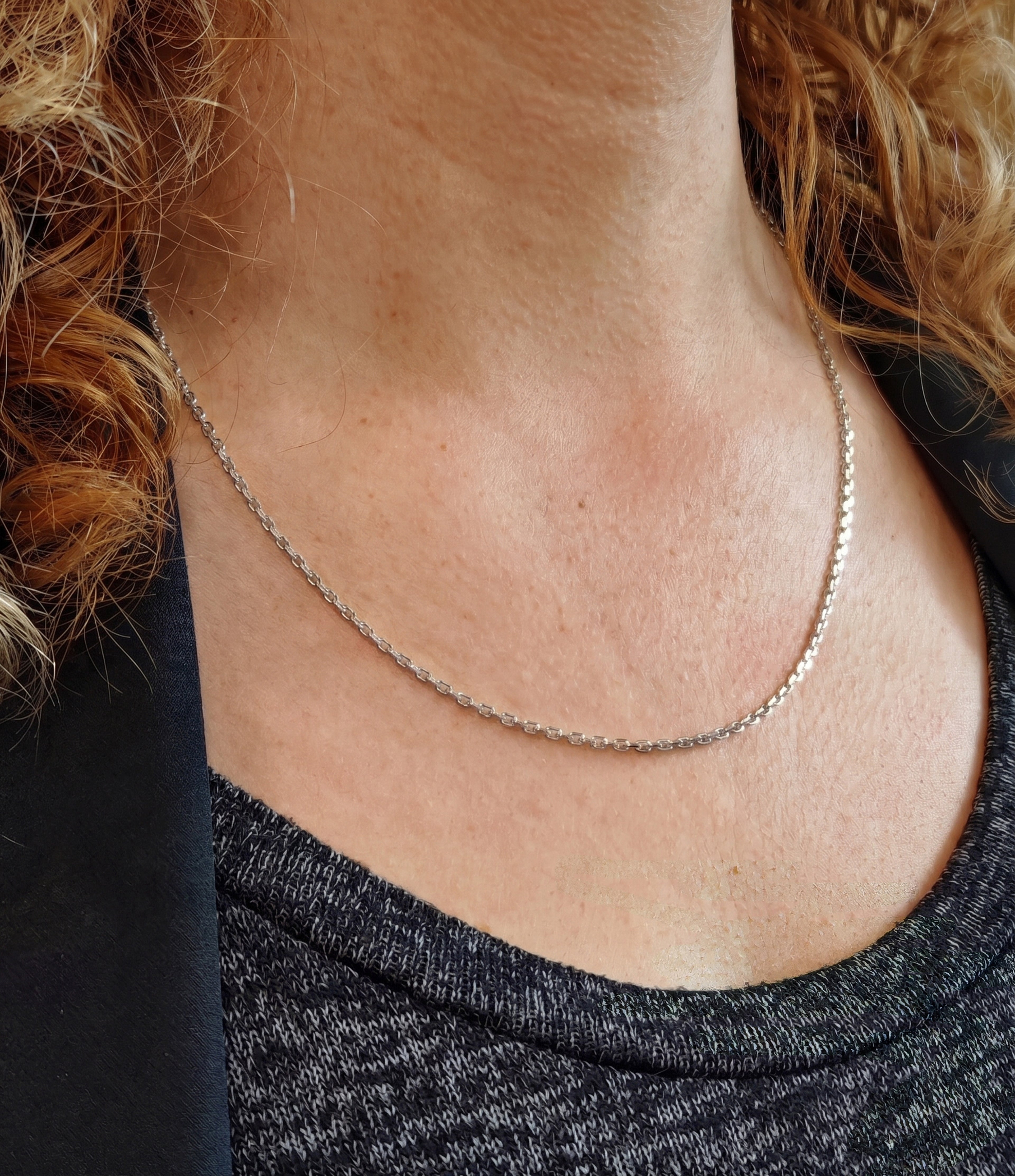 Chaine en or blanc 18 carats portée sur le cou d'une femme blonde avec bouclés et habillée en noire avec une veste de costume