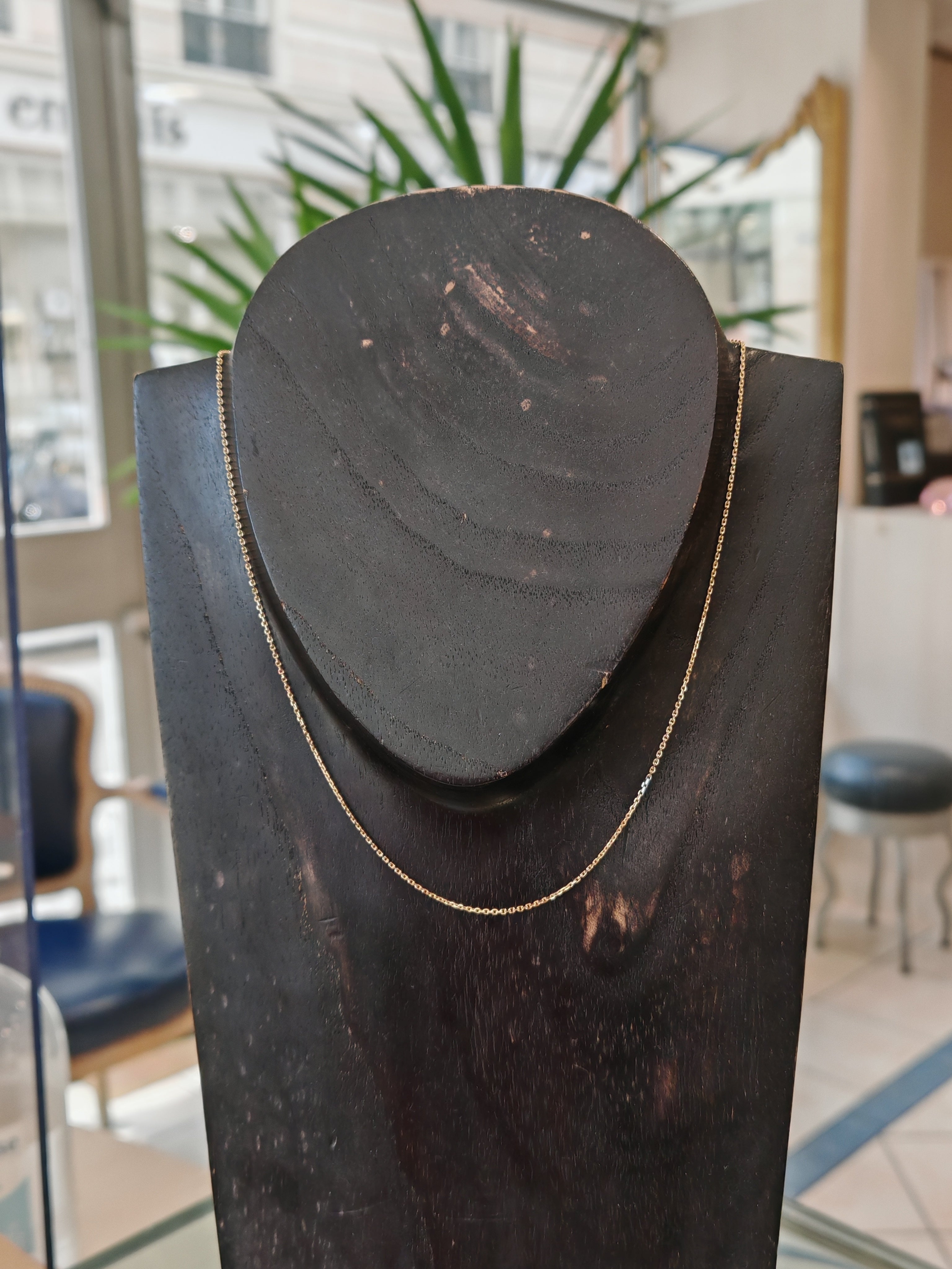 Chaine en or forçat limée en or jaune 18 carats sur un bustier en bois noir en premier plan, en second plan on y voit l'accueil d'une belle bijouterie