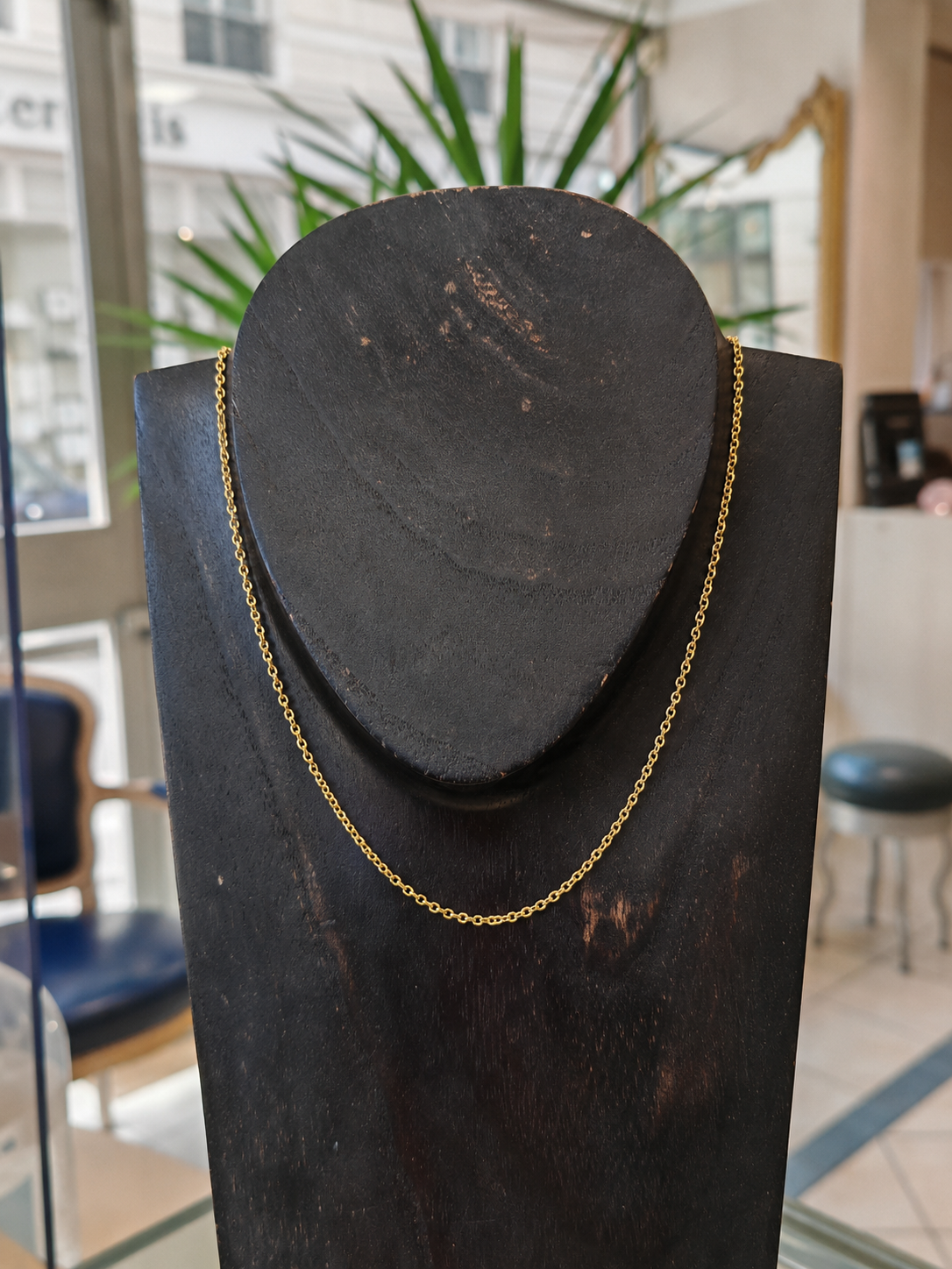 Chaine en or lentilles en or jaune 18 carats sur un bustier en bois noir en premier plan, en second plan on y voit l'accueil d'une belle bijouterie