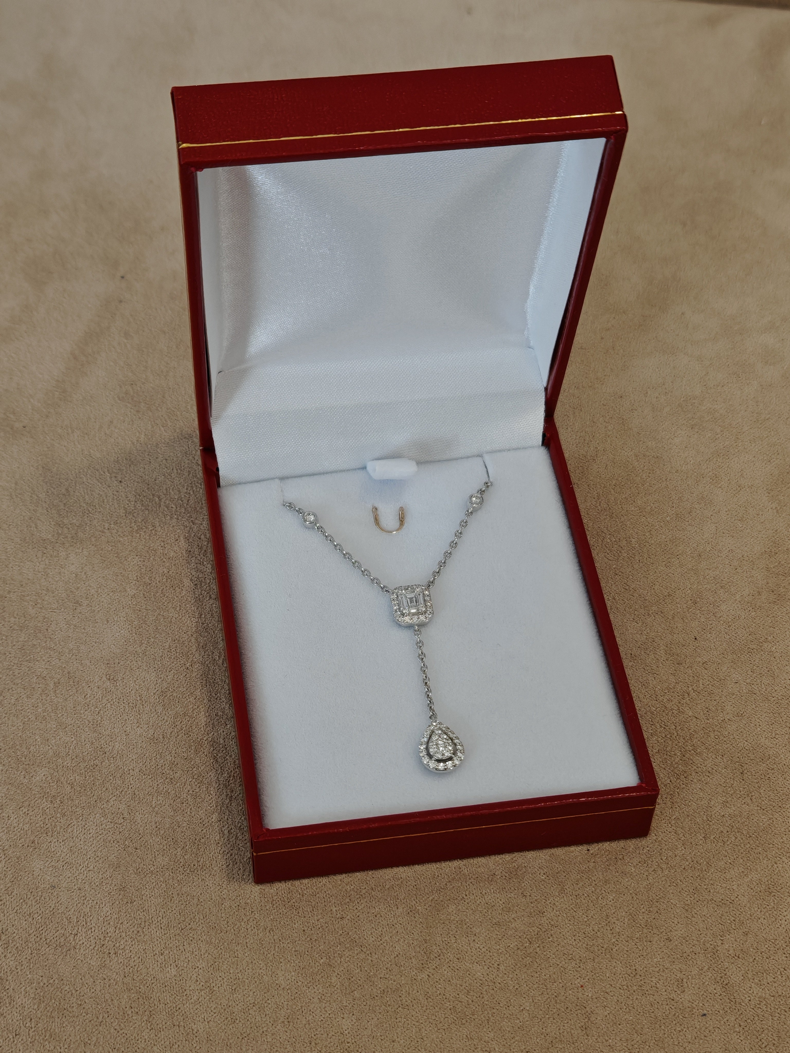 Collier en or 18 carats avec diamants carrée et poire dans un écrin rouge sur un plateau en velours