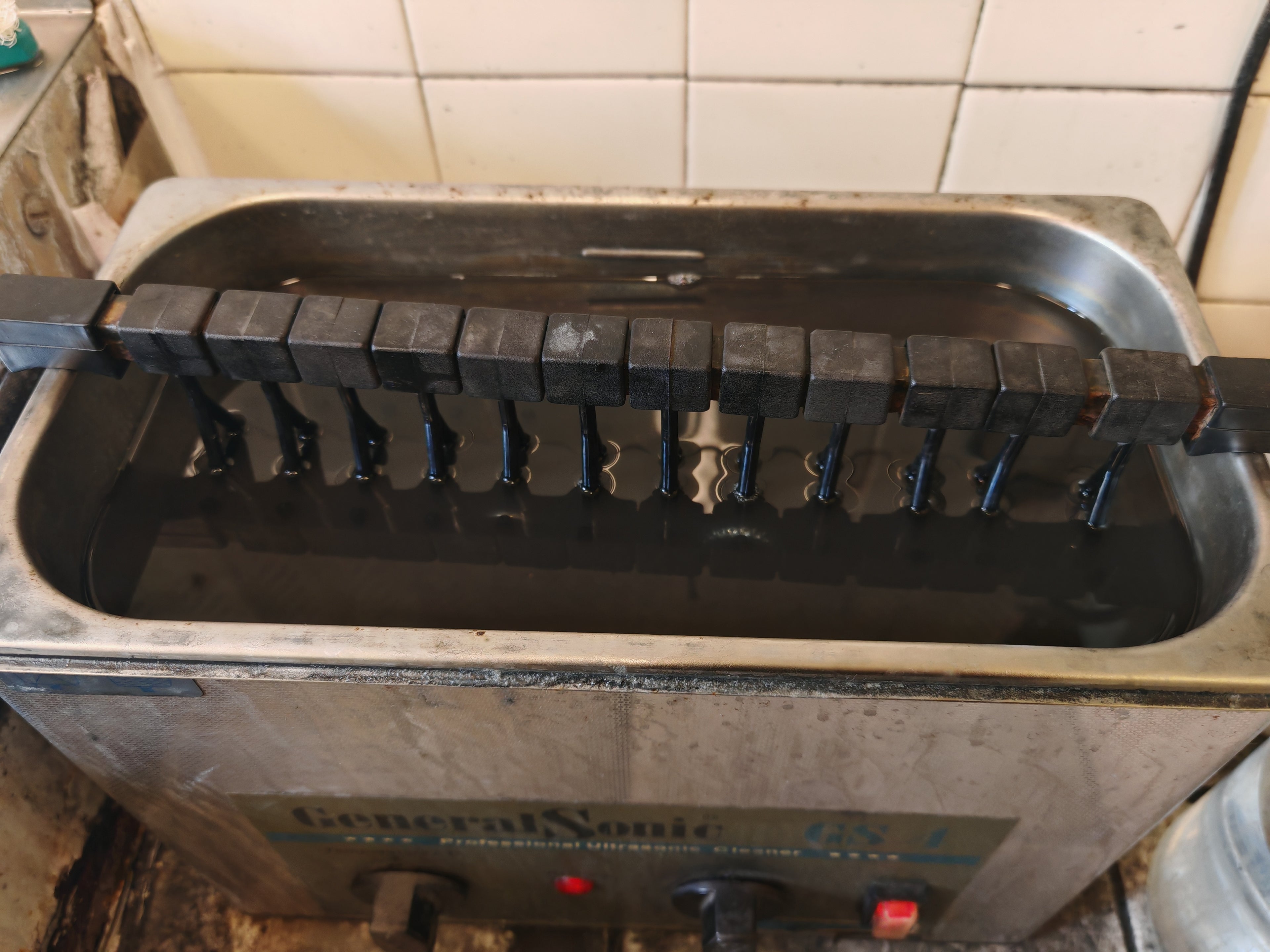 Vue du dessus d'une bassine d'ultrason avec une bague en or blanc plongée dedans.