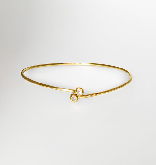 Bracelet jonc en or jaune 18 carats serti de deux diamants sur un fond blanc